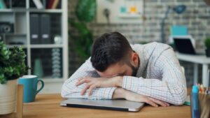 A man sits at his desk with his head in his hands, a common picture of burnout at work