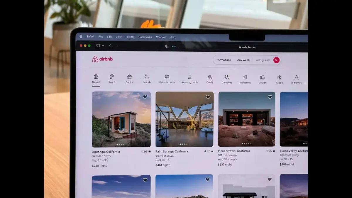 A laptop displaying the Airbnb website, showing a selection of rental listings.