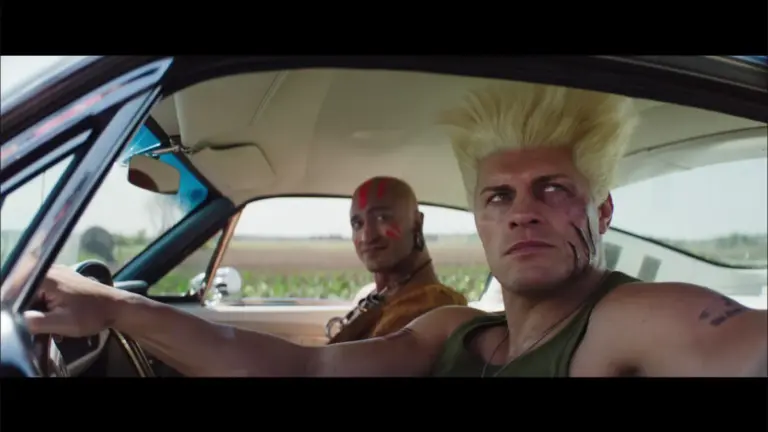 Cody Rhodes as Guile in a car sitting next to another man.