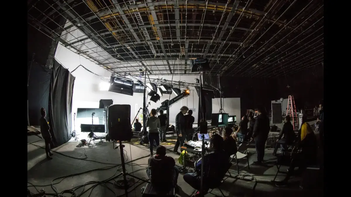 A film or television studio set with various lighting and camera equipment, crew members, and a backdrop. Fusebox Entertainment
