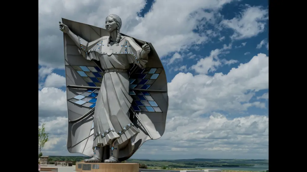 Statue of a woman in a flowing outfit, with wings made of blue and silver materials, set against a cloudy sky.