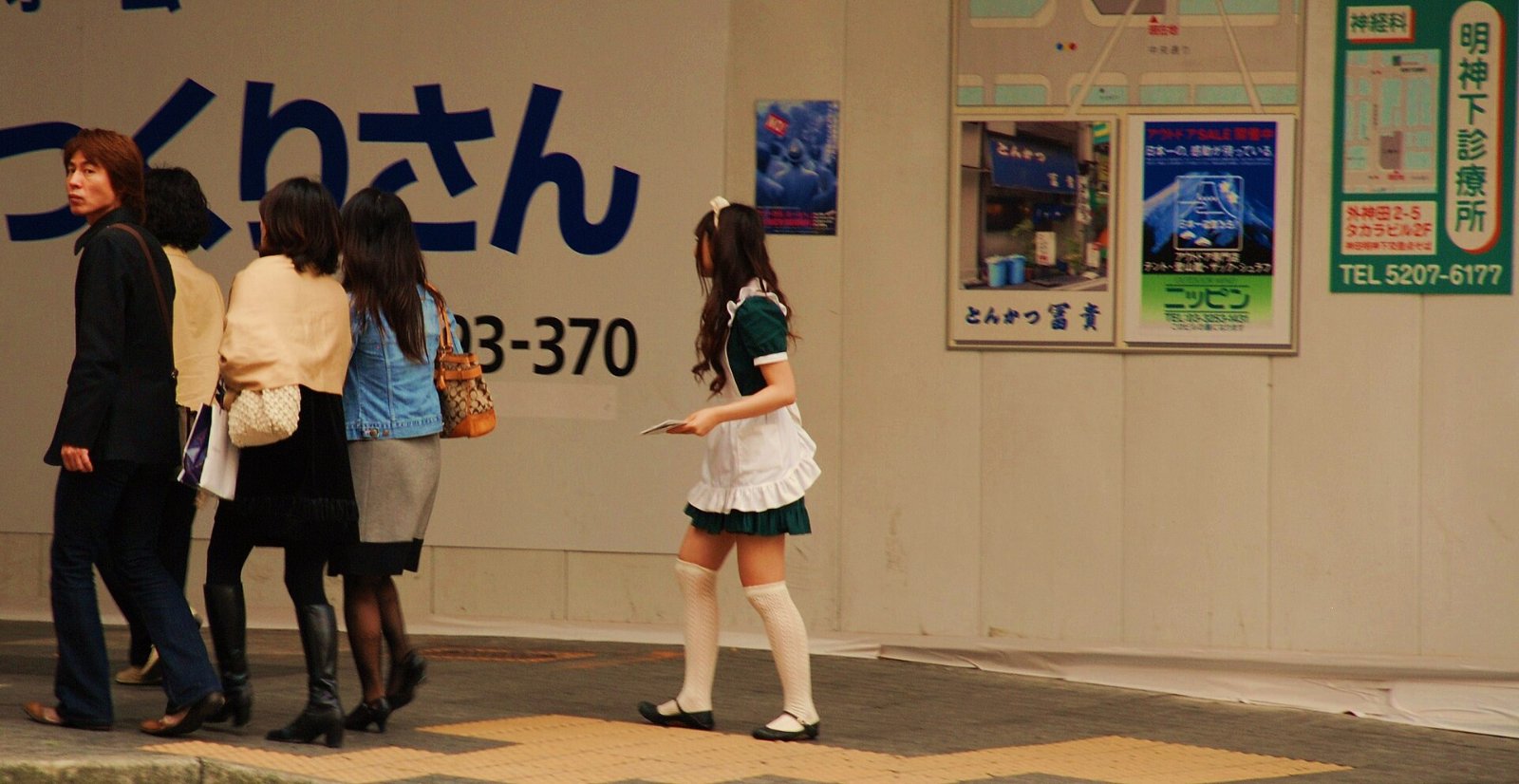 A woman in a maid uniform walks through Tokyo’s Akihabara district; the Dismissed Supermaid anime follows a maid heroine