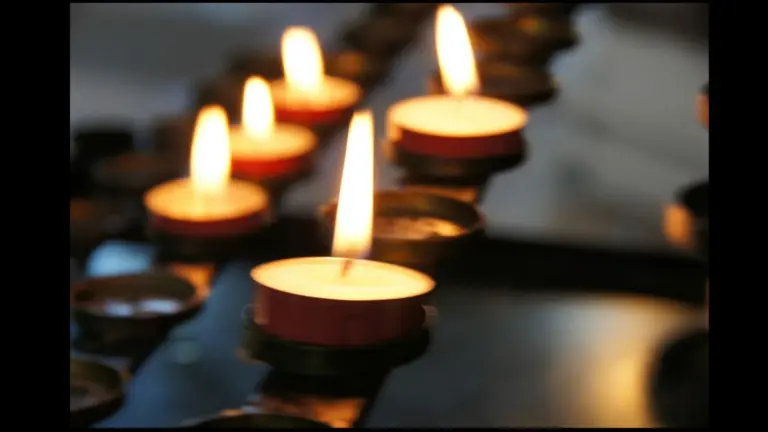 A close-up of several lit candles with flickering flames, arranged in holders.