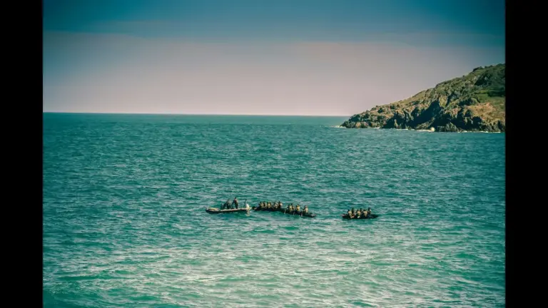 A group of people in a small boat on the water, with a rocky coastline in the background and a clear sky. Djibouti migrant boat capsizing