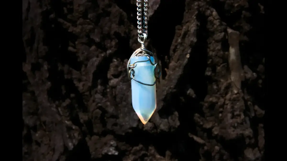 An opal pendant hanging from a silver chain against a dark, textured background.