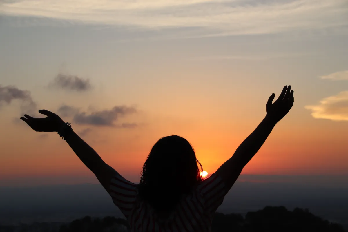 In Thursday's daily devotional, a woman lifts her hands to the sky as she views a beautiful sunset.