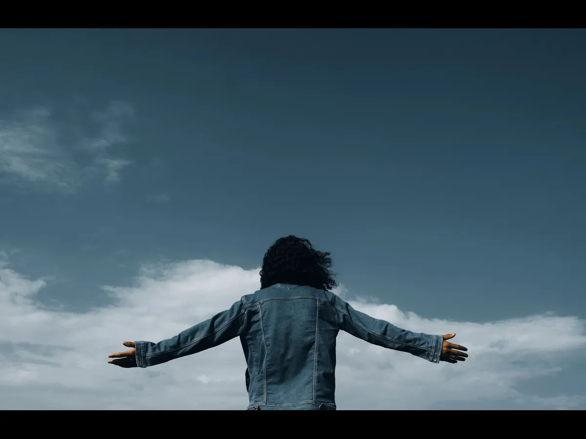 In Wednesday's daily devotional, a woman spread her arms outward in worship before a blue sky with clouds.
