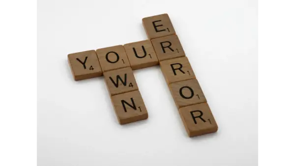 Wooden Scrabble tiles forming the motivational phrase “Own Your Error” on a white background, highlighting common misheard phrases in everyday language.