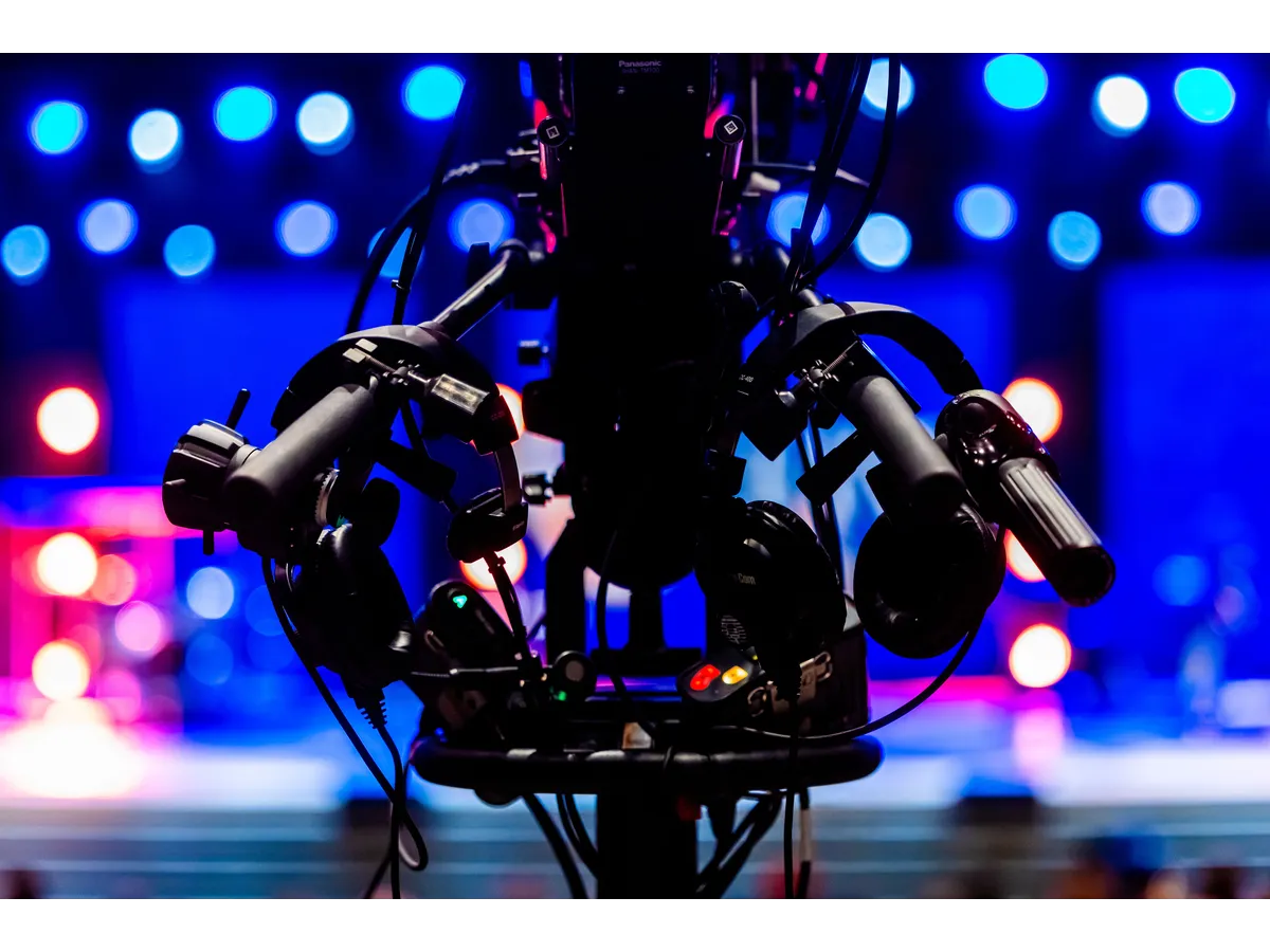 Silhouette of a professional video camera with colorful stage lights in the background, representing the televised world of famous game show scandals that captivated and shocked audiences.