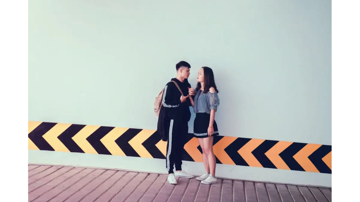 A young couple interacting by a modern wall with diagonal patterns, sharing a moment that highlights genuine couple communication.