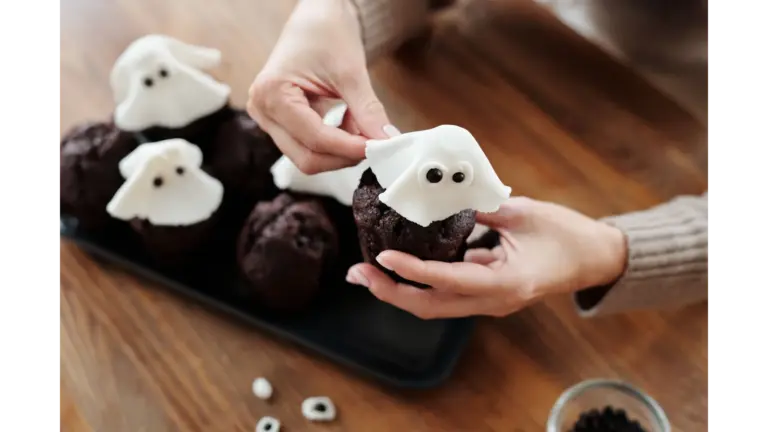Easy Halloween Cupcakes decorated as ghosts with white fondant coverings and candy eyes on chocolate cupcakes arranged on a baking tray.