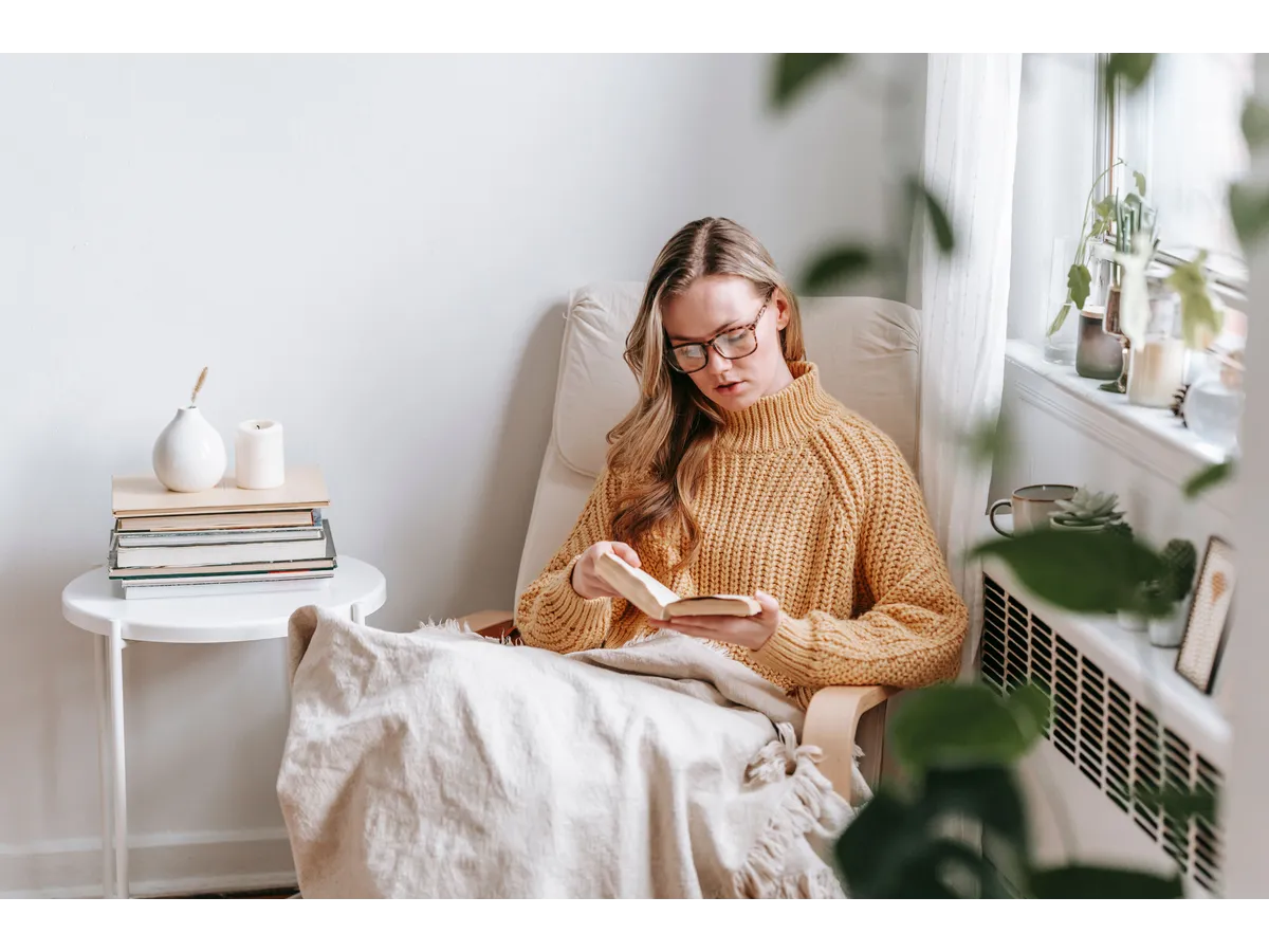Woman enjoys reading in a cozy corner filled with natural light and indoor plants, highlighting Cozy Winter Decor that creates a warm and relaxing atmosphere.