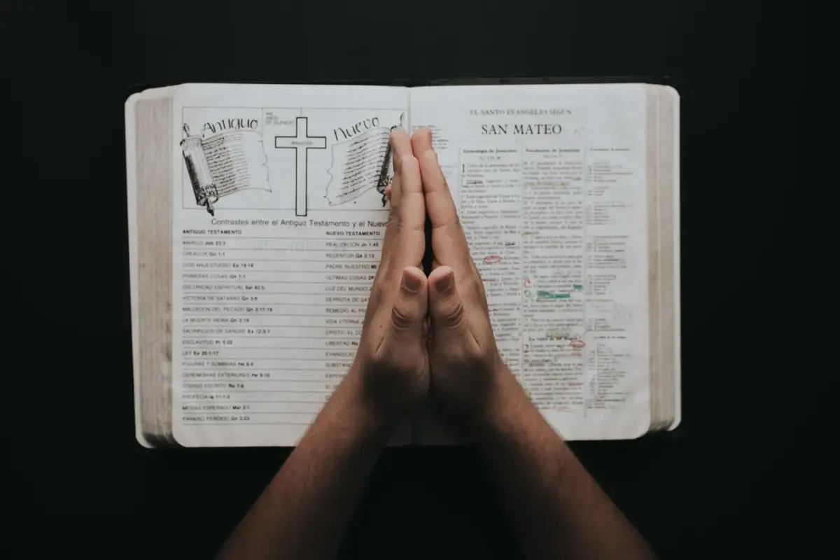 In Thursday's daily devotional, a woman's praying hands are seen atop an open Bible against a black background.