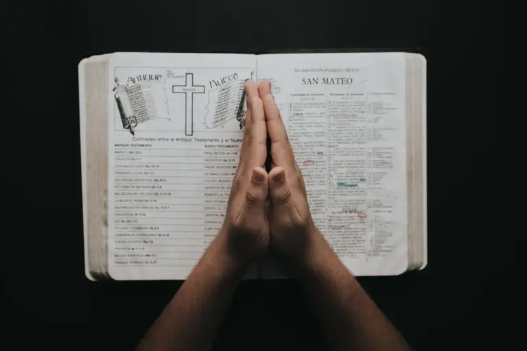 In Thursday's daily devotional, a woman's praying hands are seen atop an open Bible against a black background.