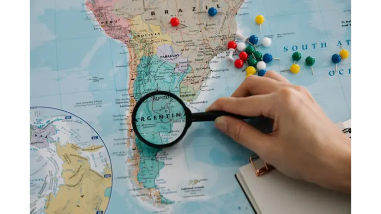 Close-up of a hand examining a South America map with a magnifying glass, highlighting Argentina, a useful detail for holiday travelers planning their next adventure.