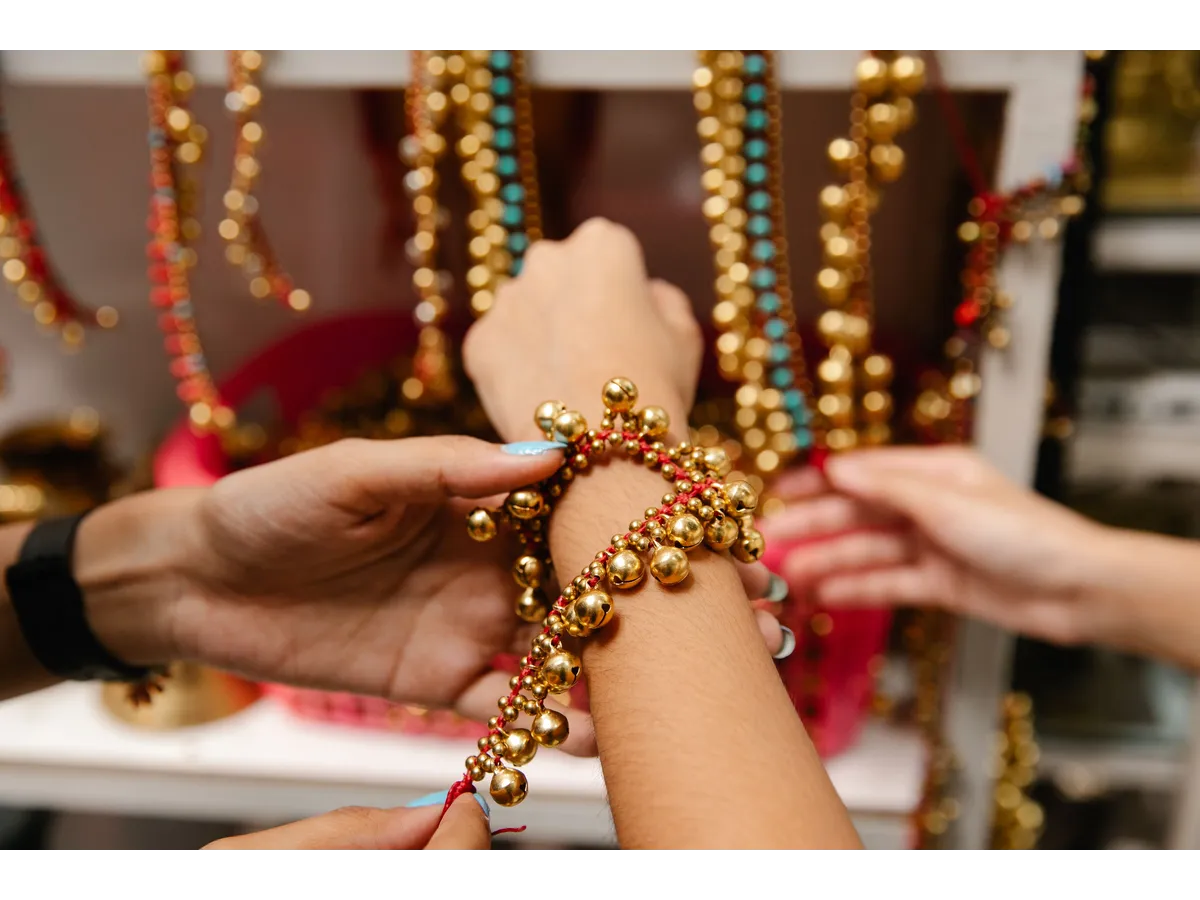 Hands arrange a vibrant gold and red beaded bracelet with colorful beads in the background, highlighting the creativity and craftsmanship behind many DIY success stories.