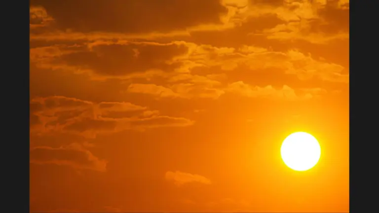 A bright sun setting against a backdrop of orange and yellow skies with scattered clouds.