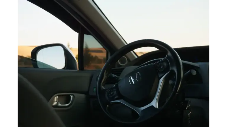 Automotive Safety Evolved View from inside a Honda car, with the steering wheel and side mirror framing a sunlit rural landscape; the quiet scene feels calm and still.