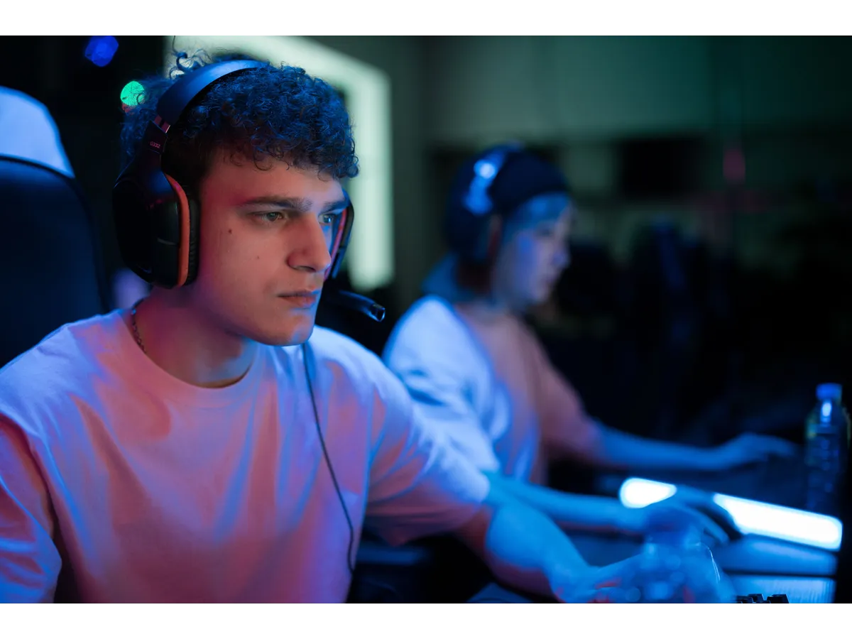Focused gamer wearing a headset plays at a computer under neon blue and pink lighting, illustrating misheard phrases in gaming voice chat.