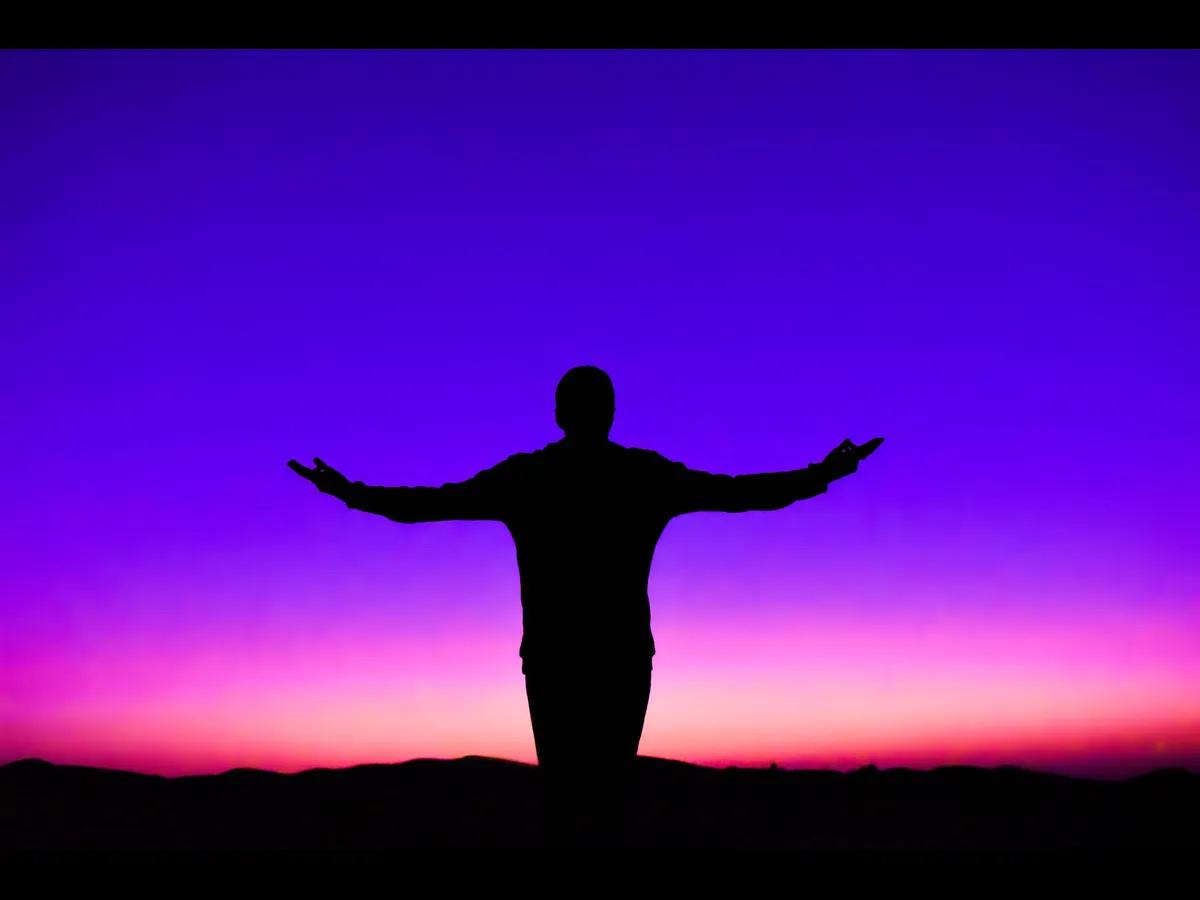 In Monday's daily devotional, a man's silhouette is seen with his arms outstretched before a colorful sunset.