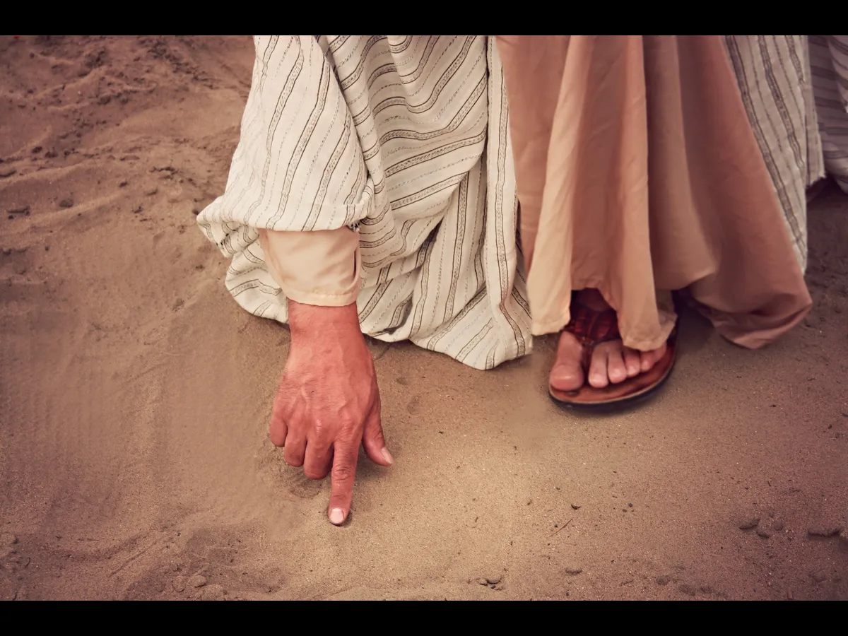 In Thursday's daily devotional, a man, wearing attire of Jesus' day, stoops and writes on the sand