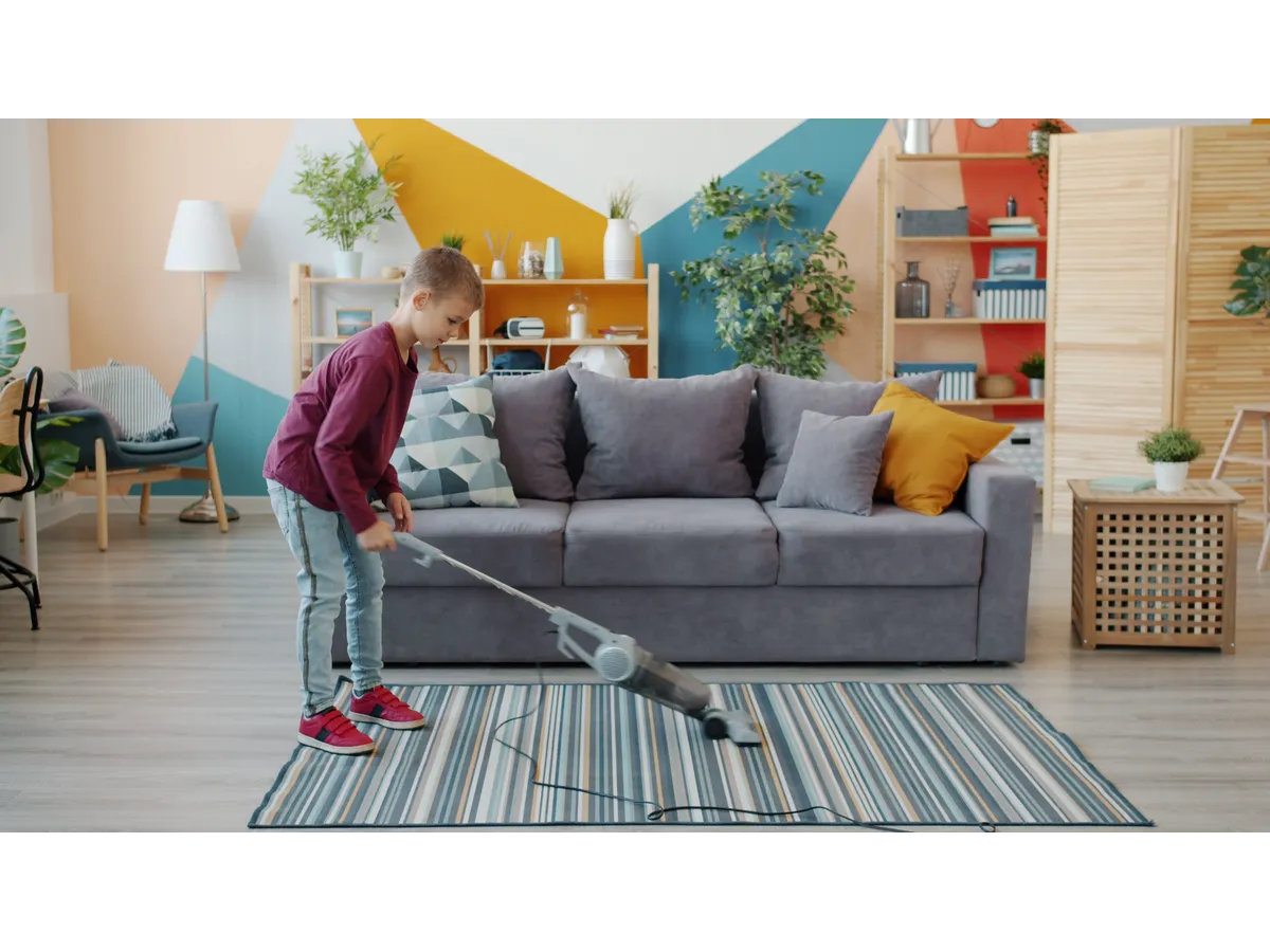 Young boy vacuuming the carpet in a colorful, modern living room, showing everyday kids chore motivation in action.