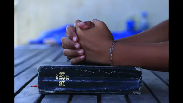 In Thursday's daily devotional, a man's hands are clasped together in prayer over a large, black Bible.