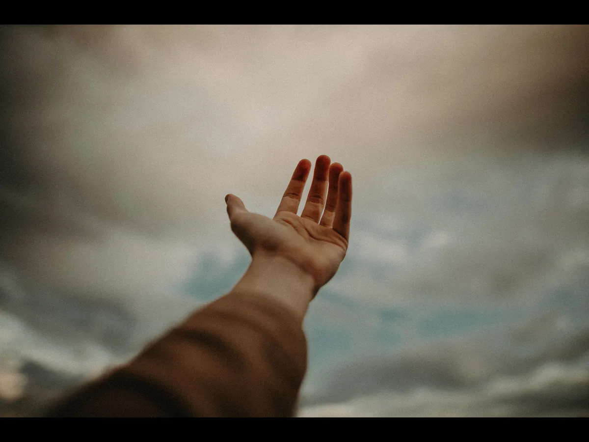 In Friday's daily devotional, a man's hand extended to heaven is seen against a cloudy sky.