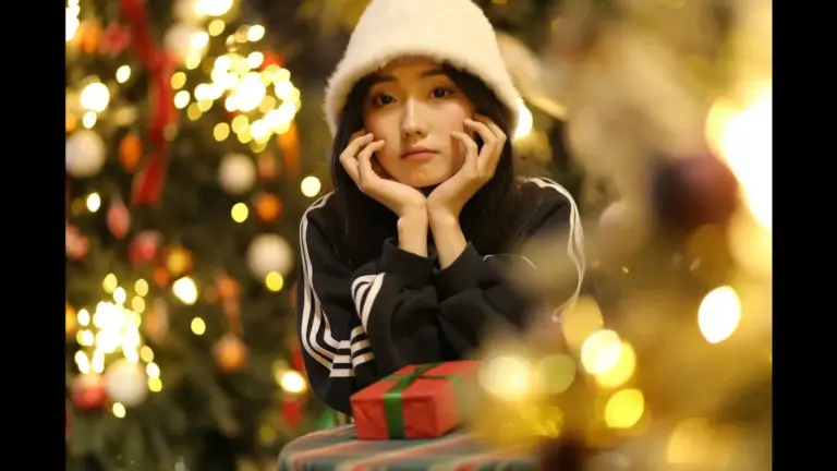 A young woman wearing a white hat resting her chin on her hands, sitting at a table with a wrapped gift, with Christmas trees and lights in the background. holiday stress
